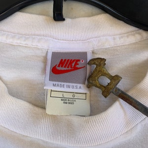 May include: White Nike t-shirt with a red Nike logo and a tag that says "Made in U.S.A. RN# 56323" and "L G".