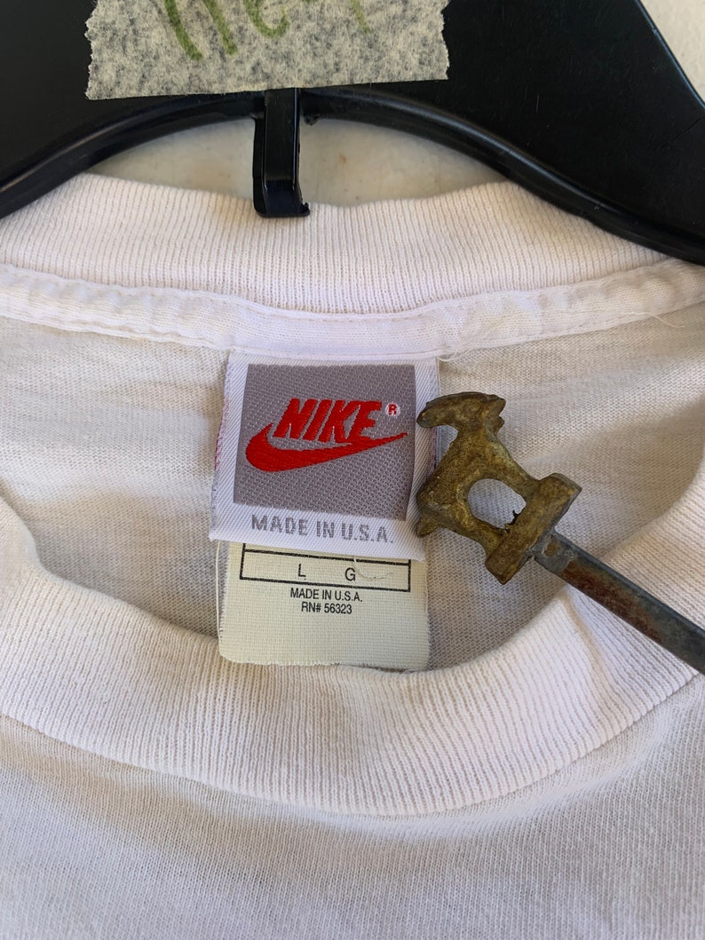 May include: White Nike t-shirt with a red Nike logo and a tag that says "Made in U.S.A. RN# 56323" and "L G".