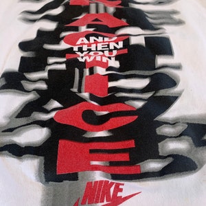 May include: White t-shirt with a black and white graphic design of the word "JUST DO IT" with the words "AND THEN YOU WIN" in red. The Nike swoosh logo is in red at the bottom.