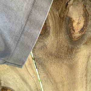 May include: Close-up of a light grey fabric with a seam running down the centre. The fabric is partially covering a piece of wood with a knot and grain pattern.