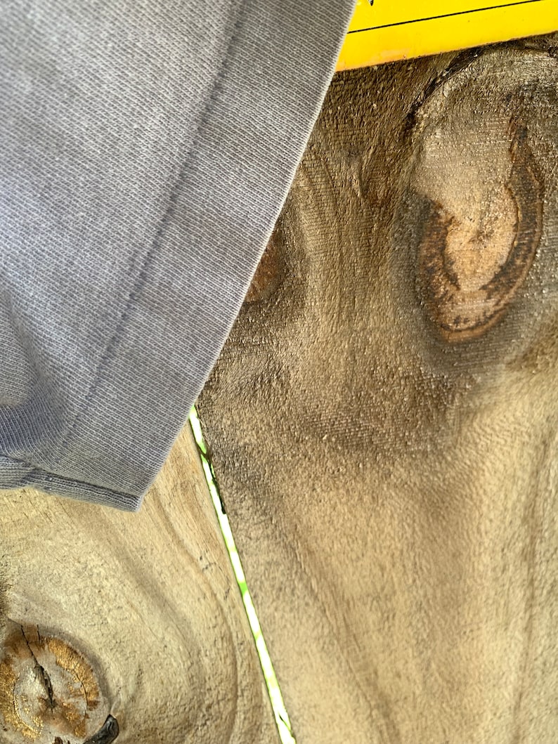 May include: Close-up of a light grey fabric with a seam running down the centre. The fabric is partially covering a piece of wood with a knot and grain pattern.