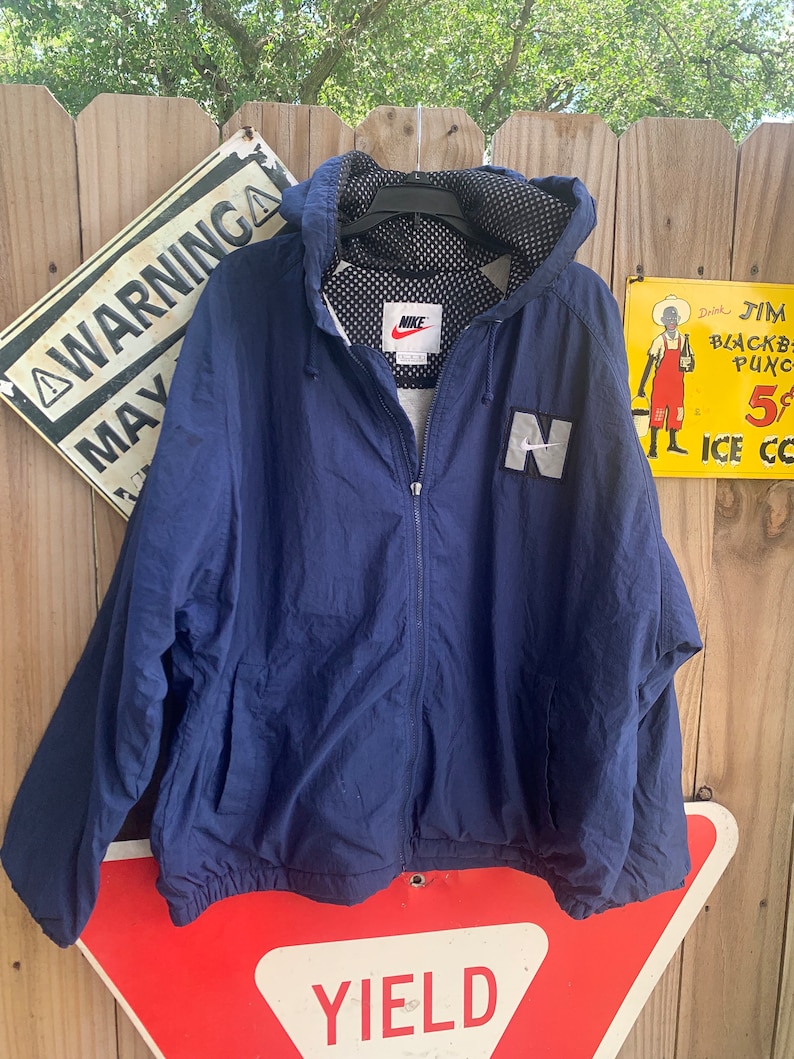 May include: A navy blue hooded jacket with a white Nike logo and a white "N" on the front. The jacket has a mesh lining and a zip closure.