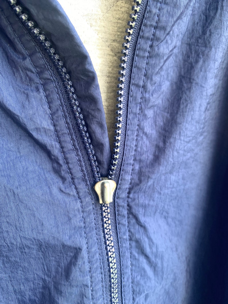May include: A navy blue zipper on a jacket. The zipper is metal and has a silver finish.