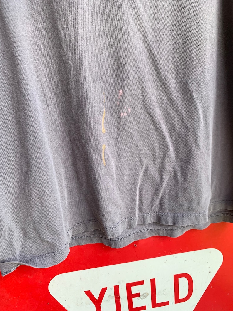 May include: A close-up of a grey t-shirt with a light brown stain and a pink stain. The t-shirt is folded and the bottom edge is visible.