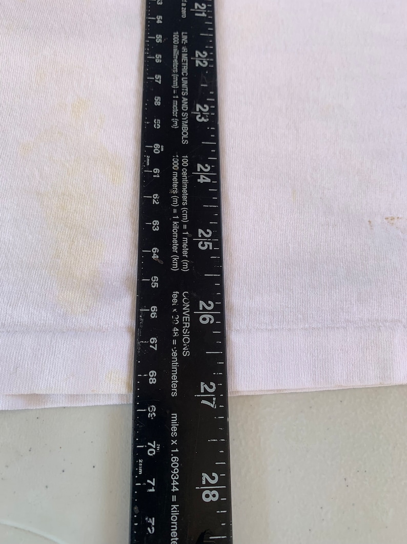 May include: A black ruler with white markings and the words "LINS AR METRIC UNITS AND SYMBOLS" and "CONVERSIONS" printed on it. The ruler measures up to 28 inches or 71 centimeters.