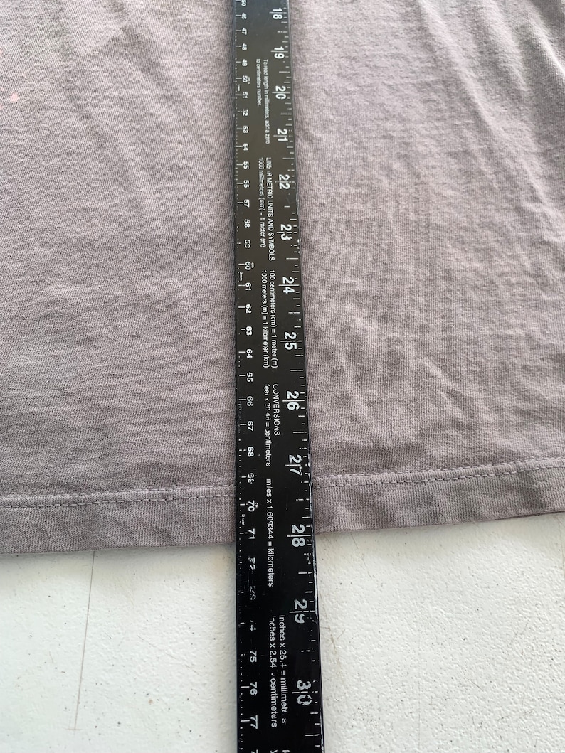 May include: A grey t-shirt with a seam along the bottom edge. A ruler is placed next to the shirt, showing the length of the shirt is 73.66 cm.