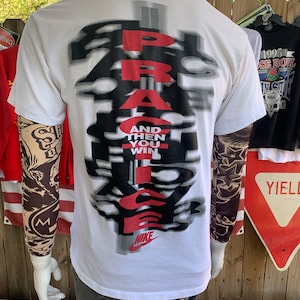 May include: White t-shirt with a black and red graphic that says "PRACTICE AND THEN YOU WIN" with a Nike swoosh logo at the bottom.