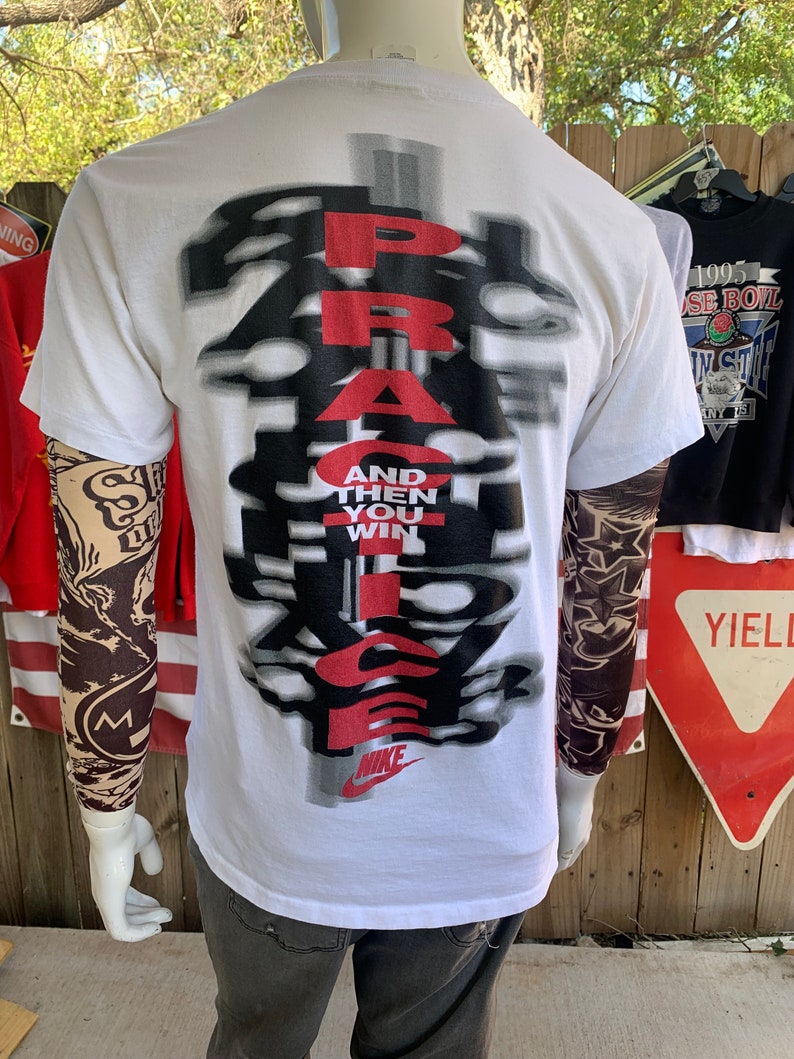 May include: White t-shirt with a black and red graphic that says "PRACTICE AND THEN YOU WIN" with a Nike swoosh logo at the bottom.