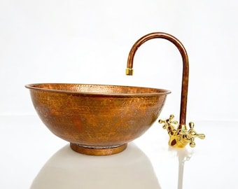Könnte beinhalten: Ein gehämmertes Kupfer-Waschbecken mit einem vergoldeten Wasserhahn. Das Waschbecken ist oval geformt und hat eine strukturierte Oberfläche. Der Wasserhahn hat zwei vergoldete Griffe.