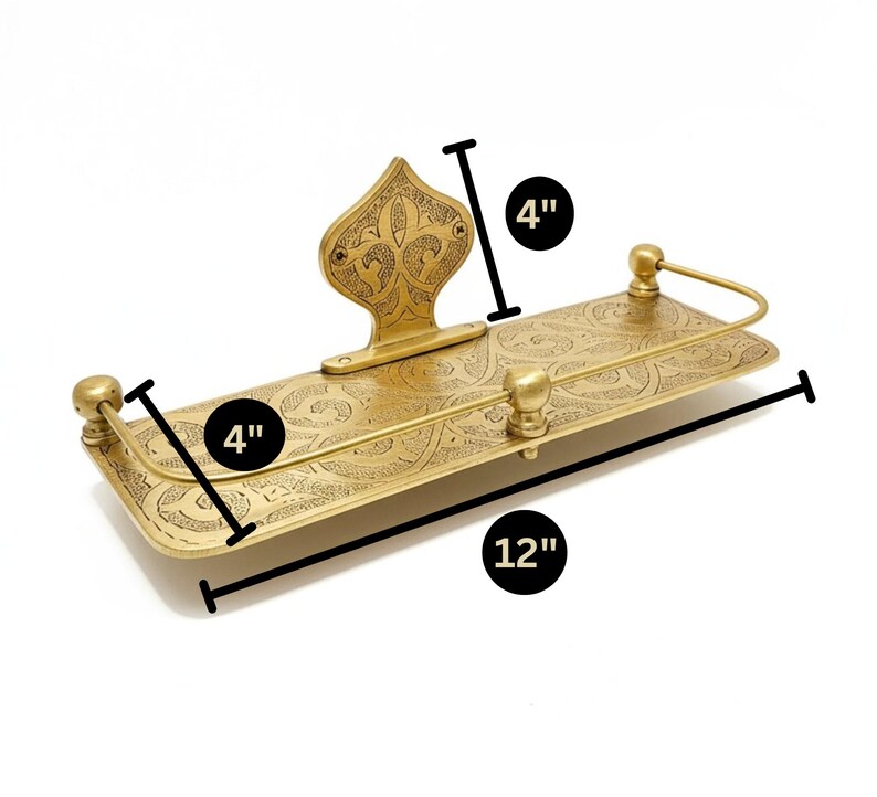 Puede incluir: Una estanter&iacute;a rectangular de color lat&oacute;n con un dise&ntilde;o grabado y ornamentado. La estanter&iacute;a mide 30 cm de largo y 10 cm de ancho, con una pieza trasera decorativa y detalles redondeados. La estanter&iacute;a mide 10 cm de alto. El dise&ntilde;o es probablemente para ba&ntilde;o o cocina.