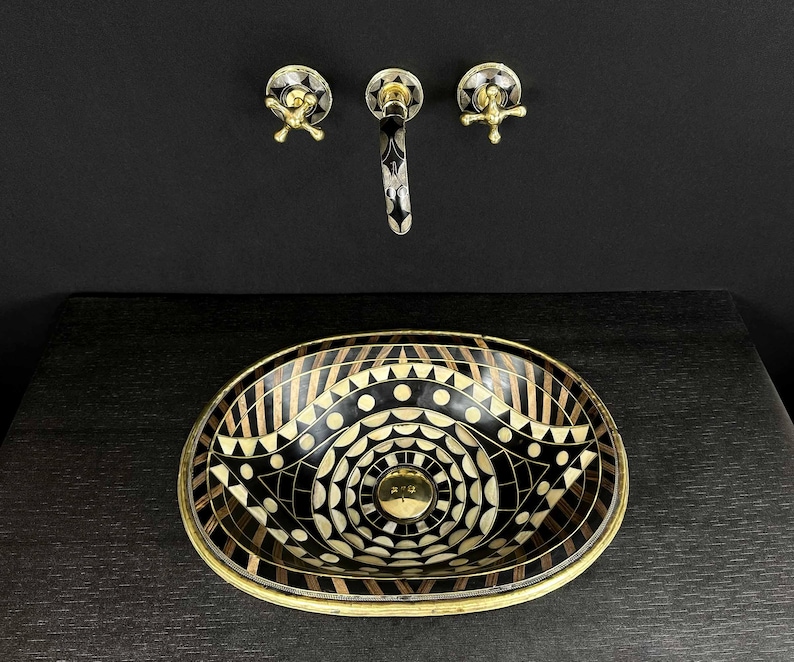 K&ouml;nnte beinhalten: Ein ovales Waschbecken in Schwarz und Wei&szlig; mit einem geometrischen Muster. Das Waschbecken hat einen Messingrand und steht auf einer schwarzen Arbeitsplatte. Ein Messinghahn mit schwarzem Griff ist an der Wand &uuml;ber dem Waschbecken montiert.