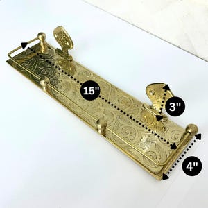 Puede incluir: Un estante de metal dorado con un dise&ntilde;o floral ornamentado. El estante mide 38 cm de largo, 10 cm de ancho y 8 cm de alto. Tiene dos soportes decorativos y detalles en forma de bola. El estante est&aacute; dise&ntilde;ado para montarse en la pared.
