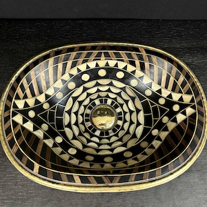 K&ouml;nnte beinhalten: Ein ovales Dekorbrett mit einem geometrischen Muster in Schwarz und Wei&szlig;. Das Tablett hat einen Messingrand und ein Messing-Mittelst&uuml;ck.