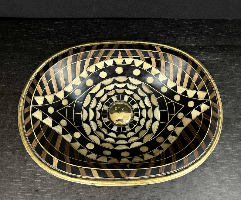 K&ouml;nnte beinhalten: Ein ovales Dekorbrett mit einem geometrischen Muster in Schwarz und Wei&szlig;. Das Tablett hat einen Messingrand und ein Messing-Mittelst&uuml;ck.