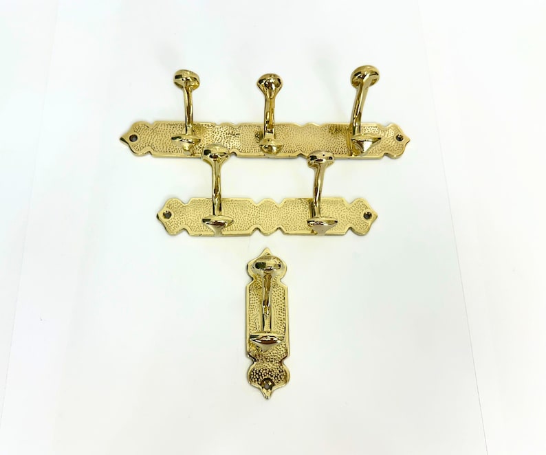 Pode incluir: Um conjunto de tr&ecirc;s cabides de lat&atilde;o e um gancho &uacute;nico. Os cabides t&ecirc;m uma superf&iacute;cie texturizada e extremidades decorativas. Cada cabide tem v&aacute;rios ganchos curvos. O gancho &uacute;nico tem um design semelhante.
