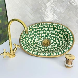 May include: A green and white oval sink with a brass faucet and drain stopper. The sink has a pattern of white circles on a green background.