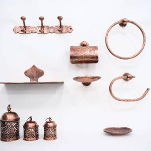 Puede incluir: Un conjunto de accesorios de baño de cobre, que incluye un toallero, un porta rollo de papel higiénico, un jabonera, un porta cepillos de dientes y una estantería. Los accesorios están todos decorados con intrincados patrones.