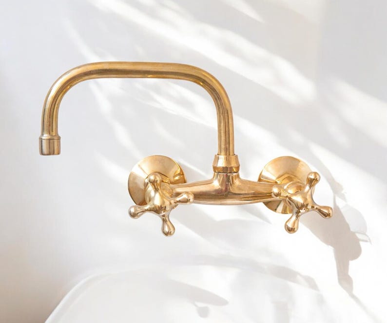 May include: A gold-toned brass wall-mounted faucet with two cross-shaped handles.