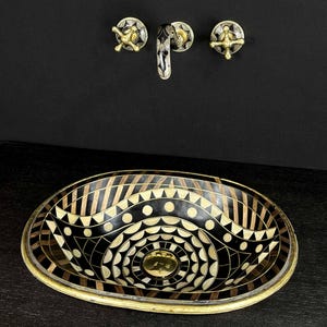 K&ouml;nnte beinhalten: Ovales Waschbecken mit geometrischem Muster in Schwarz und Gold. Das Waschbecken besteht aus einer Mosaik aus verschiedenen Materialien, darunter Holz, Metall und Stein. Das Waschbecken ist vor einem schwarzen Hintergrund platziert.
