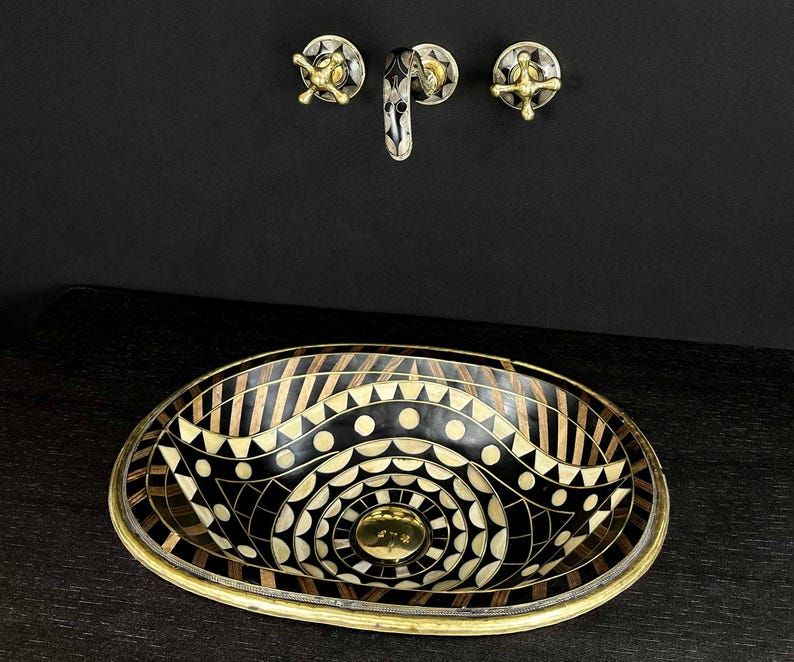 K&ouml;nnte beinhalten: Ovales Waschbecken mit geometrischem Muster in Schwarz und Gold. Das Waschbecken besteht aus einer Mosaik aus verschiedenen Materialien, darunter Holz, Metall und Stein. Das Waschbecken ist vor einem schwarzen Hintergrund platziert.
