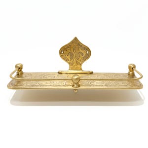Puede incluir: Estante rectangular de color lat&oacute;n con un dise&ntilde;o floral ornamentado. El estante tiene una placa trasera decorativa y dos peque&ntilde;os tiradores curvos. Un peque&ntilde;o pomo redondo est&aacute; centrado en la parte delantera.