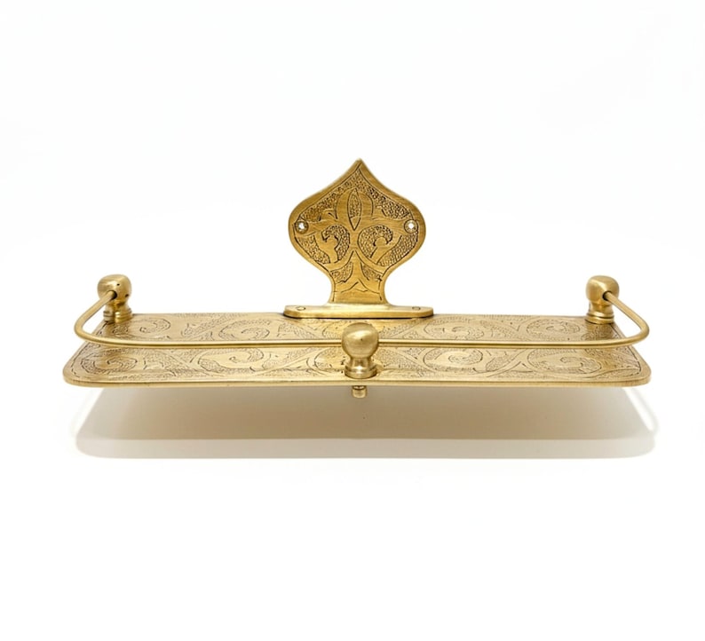 Puede incluir: Estante rectangular de color lat&oacute;n con un dise&ntilde;o floral ornamentado. El estante tiene una placa trasera decorativa y dos peque&ntilde;os tiradores curvos. Un peque&ntilde;o pomo redondo est&aacute; centrado en la parte delantera.
