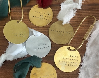 May include: A collection of round, metallic keychains with stamped text, including phrases like "Favorite Grandma" and "Christmas in the Northwest." Each keychain is attached to a ribbon in various colors, such as white, red, and green.