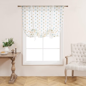 Może przedstawiać: Przezroczysta biała zasłona okienna z kolorowymi kropkami w kolorze niebieskim, pomarańczowym i zielonym. Zasłona jest zawiązana pośrodku. Element dekoracyjny do każdego pomieszczenia.