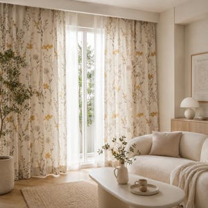 May include: Cream floral curtains with yellow and grey accents. The sheer curtains allow natural light to filter through. The design features a repeating pattern of flowers and foliage, creating a soft atmosphere. The curtains are in a living room setting.