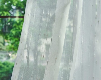 Pode incluir: Um painel de cortina branco transparente com um padrão de riscas verticais composto por pequenos pontos tufados em relevo. O tecido leve e semitransparente deixa passar a luz, realçando o design linear texturado na superfície.
