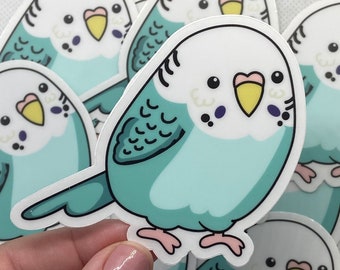 Puede incluir: Un conjunto de pegatinas de periquitos de estilo de dibujos animados coloridos. Los periquitos son de color azul claro con el vientre blanco y el pico amarillo. Tienen ojos negros y pequeños detalles morados en la cabeza. Las pegatinas están sobre un fondo blanco.