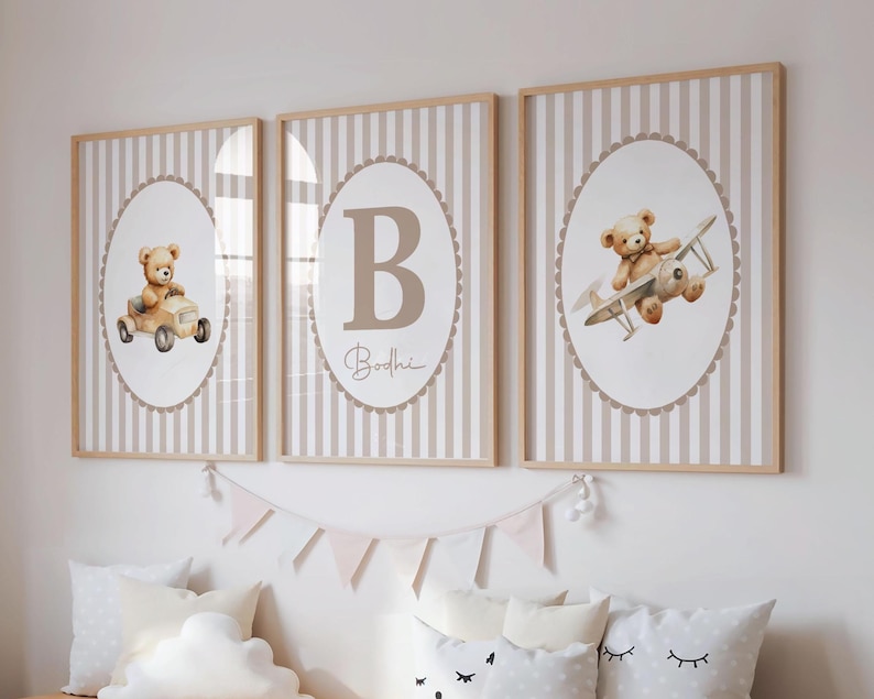 May include: Three framed nursery art prints. Each print features a beige teddy bear illustration. One print shows a teddy bear in a car, another with a plane, and the third with a large letter "B" and the name "Bodhi". The background is striped.