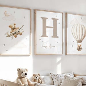Pode incluir: Tr&ecirc;s impress&otilde;es art&iacute;sticas emolduradas para o ber&ccedil;&aacute;rio. Uma apresenta um ursinho de pel&uacute;cia num biplano, outra uma grande letra "H" com o nome "Hudson", e a terceira um ursinho de pel&uacute;cia num bal&atilde;o de ar quente. Todas as impress&otilde;es t&ecirc;m uma moldura de madeira clara.