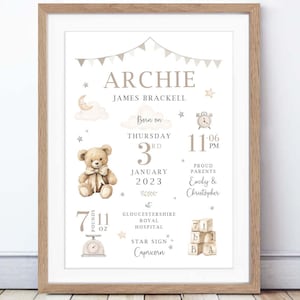 May include: A framed birth announcement print with a light brown wooden frame. The print features the name "Archie", birth details, a teddy bear illustration, and the text "7 lbs 11 oz". The design includes stars, clouds, and a banner.