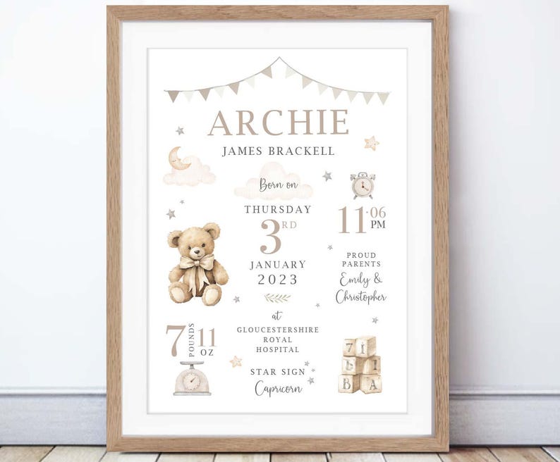 May include: A framed birth announcement print with a light brown wooden frame. The print features the name "Archie", birth details, a teddy bear illustration, and the text "7 lbs 11 oz". The design includes stars, clouds, and a banner.