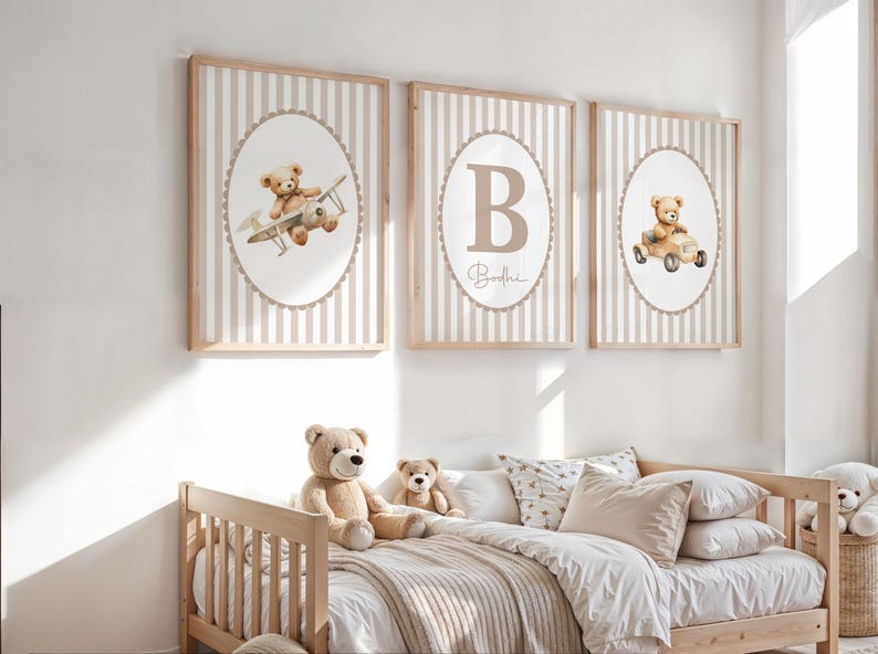 May include: Three framed nursery art prints with a teddy bear theme. Each print features a beige and white striped background with an oval illustration of a teddy bear in a plane, car, and the letter "B". The prints are in wooden frames.