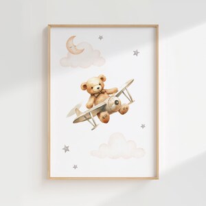 Pode incluir: Ilustra&ccedil;&atilde;o em aquarela de um urso de pel&uacute;cia pilotando um avi&atilde;o vintage, em um fundo branco com nuvens, estrelas e uma lua crescente. A obra de arte &eacute; emoldurada em uma moldura de madeira clara, ideal para decora&ccedil;&atilde;o de ber&ccedil;&aacute;rio.