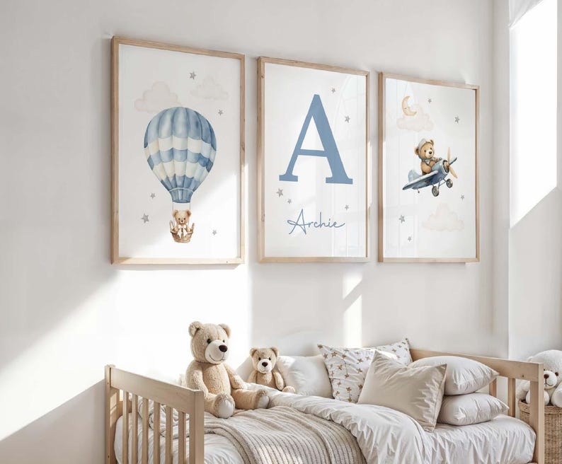 May include: Three framed nursery art prints. One features a blue and white hot air balloon with a teddy bear. Another displays a large blue letter "A" with the name "Archie". The third shows a teddy bear piloting a blue airplane.