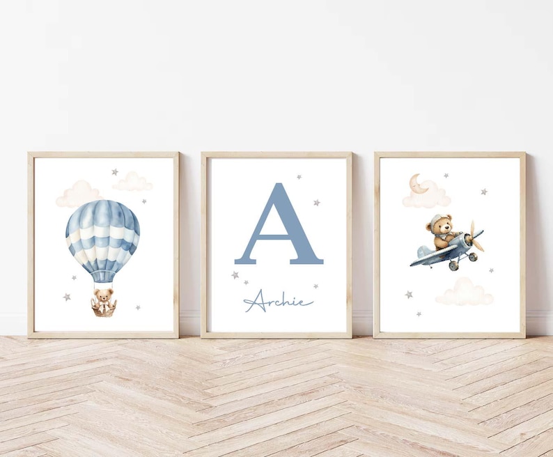 May include: Three framed nursery art prints. One features a blue and white hot air balloon with a teddy bear. Another displays the letter "A" and the name "Archie". The third shows a teddy bear in a plane.