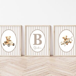 May include: Three framed nursery art prints. Each print features a watercolour illustration of a teddy bear. One bear is in a car, one is in an aeroplane, and the third has the letter "B" and the name "Bodhe". The background has a striped pattern.
