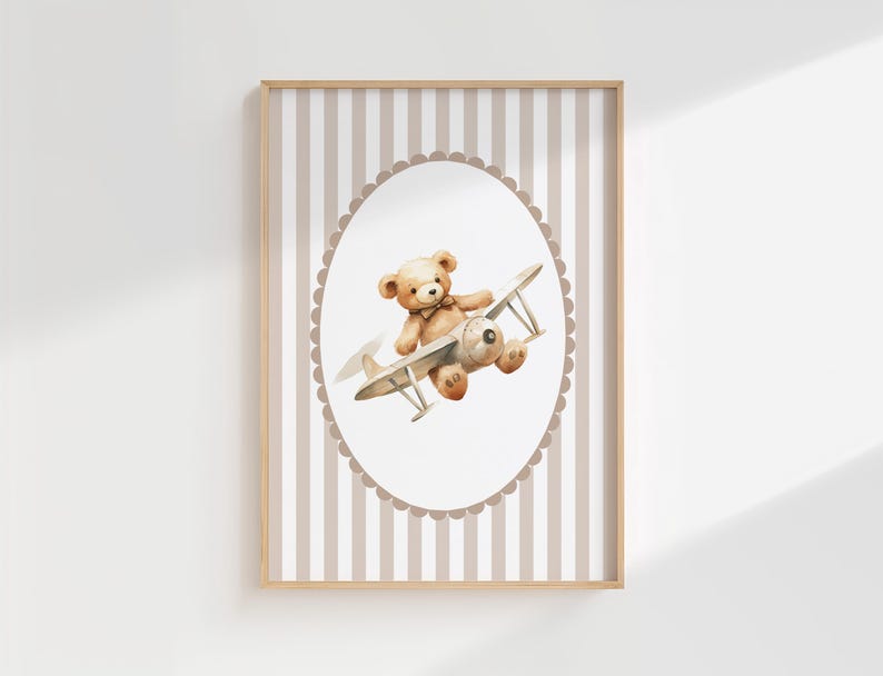 May include: A framed print with a watercolour illustration of a teddy bear flying a vintage biplane. The bear is light brown, and the plane is beige and grey. The background has vertical stripes in beige and white, with a scalloped oval frame.