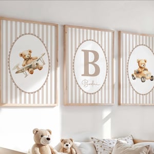 May include: Three framed nursery art prints. Each print features a beige teddy bear illustration. One print shows a bear in a plane, another with the letter "B" and the name "Bodhi", and the third with a bear in a car. The background has vertical beige and white stripes.