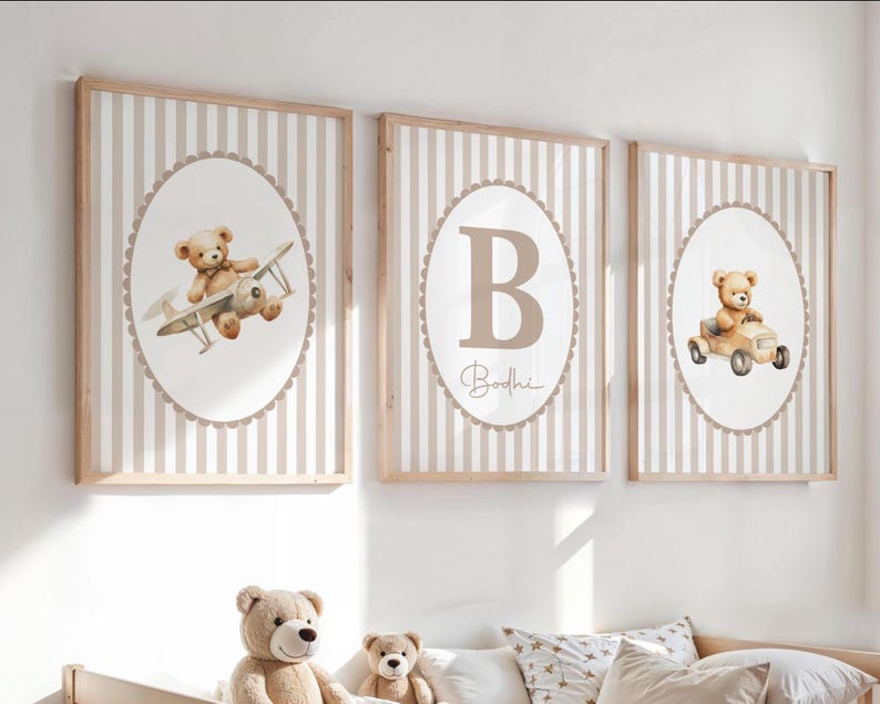 May include: Three framed nursery art prints. Each print features a beige teddy bear illustration. One print shows a bear in a plane, another with the letter "B" and the name "Bodhi", and the third with a bear in a car. The background has vertical beige and white stripes.