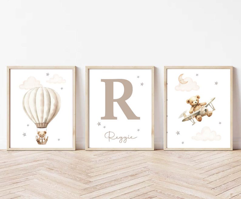 Pode incluir: Tr&ecirc;s impress&otilde;es art&iacute;sticas emolduradas para o quarto infantil. A primeira apresenta um bal&atilde;o de ar quente com um ursinho de pel&uacute;cia, a segunda uma grande letra "R" com o nome "Reggie", e a terceira um ursinho de pel&uacute;cia num biplano. Todas as impress&otilde;es t&ecirc;m uma paleta de cores neutra.