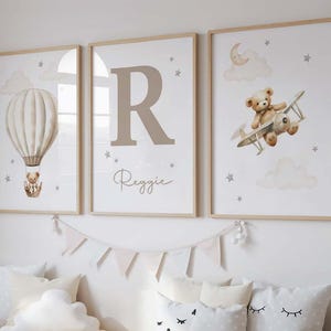 Pode incluir: Tr&ecirc;s impress&otilde;es de arte emolduradas para o ber&ccedil;&aacute;rio. Uma apresenta um bal&atilde;o de ar quente com um ursinho de pel&uacute;cia, outra exibe a letra "R" com o nome "Reggie", e a terceira mostra um ursinho de pel&uacute;cia em um biplano. Tudo em tons neutros.
