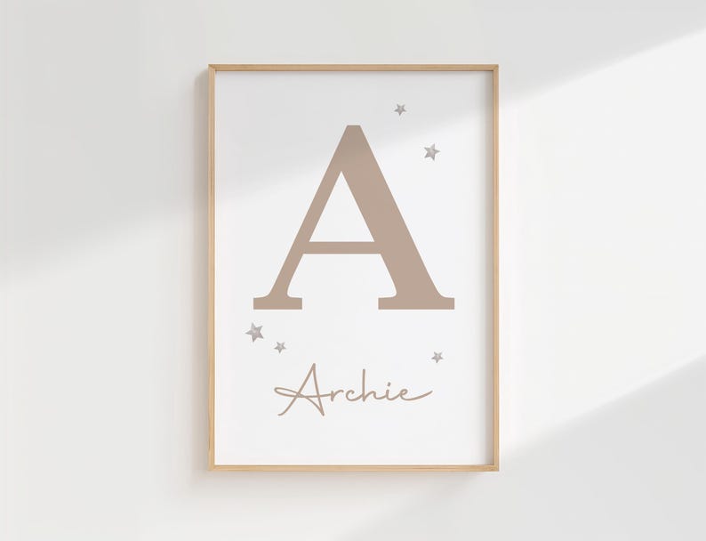 Pode incluir: Impress&atilde;o emoldurada com uma grande letra "A" em tom taupe e o nome "Archie" em escrita cursiva. Pequenas estrelas adornam a letra. A impress&atilde;o tem um fundo branco e uma moldura de madeira clara, ideal para um quarto infantil.