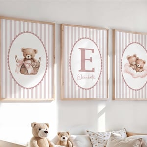 May include: Three framed nursery art prints with a pink and white striped background. Each print features a different design: a teddy bear in a basket, the letter "E" with the name "Elisabeth", and two teddy bears on a cloud.