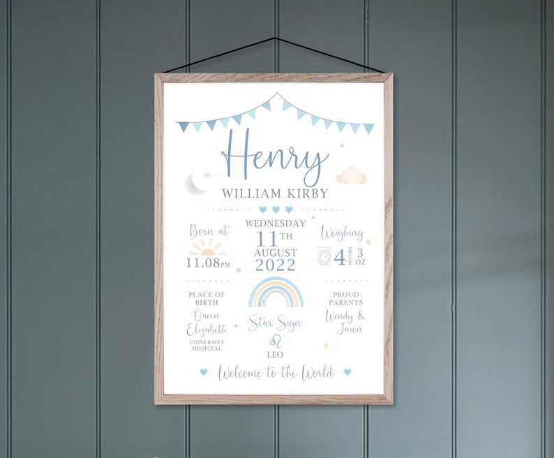 May include: A framed print with a light wood frame, featuring the name "Henry" in blue script. The print includes details like birth date, time, weight (4 lbs 3 oz), and place of birth, with decorative elements like a rainbow and clouds.