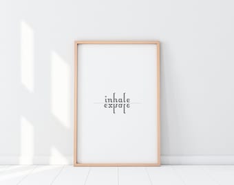 May include: A framed print with the text "inhale exhale" in black lettering on a white background. The frame is light wood.
