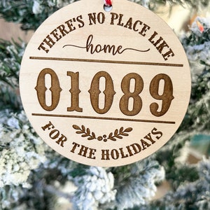 May include: A round wooden ornament with the text "There's no place like home" and the number "01089" in a decorative font. The ornament also has the text "For the Holidays" and a small wreath design.